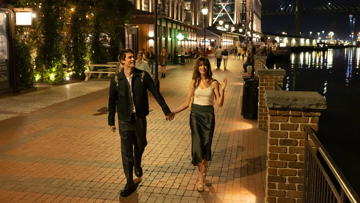 Solène and Hayes walking hand in hand along a river at night in The Idea of You